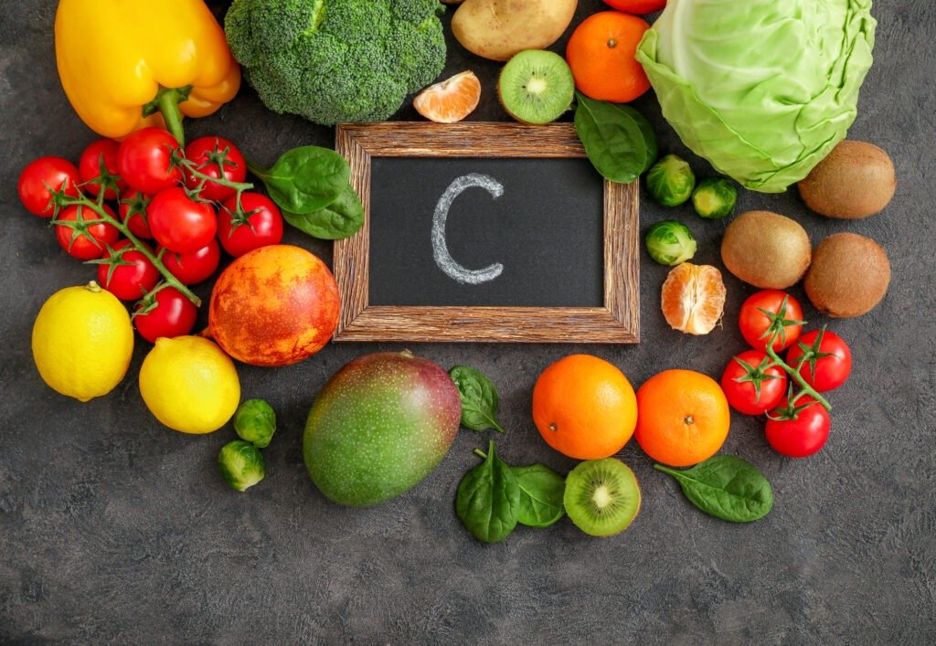 Assortment of high vitamin A sources on dark background: spinach, tomatoes, potatoes, broccoli, cabbage, Brussels sprouts, kiwi fruits, mango, granadilla, lemons, peppers, ,mandarines. Top view.