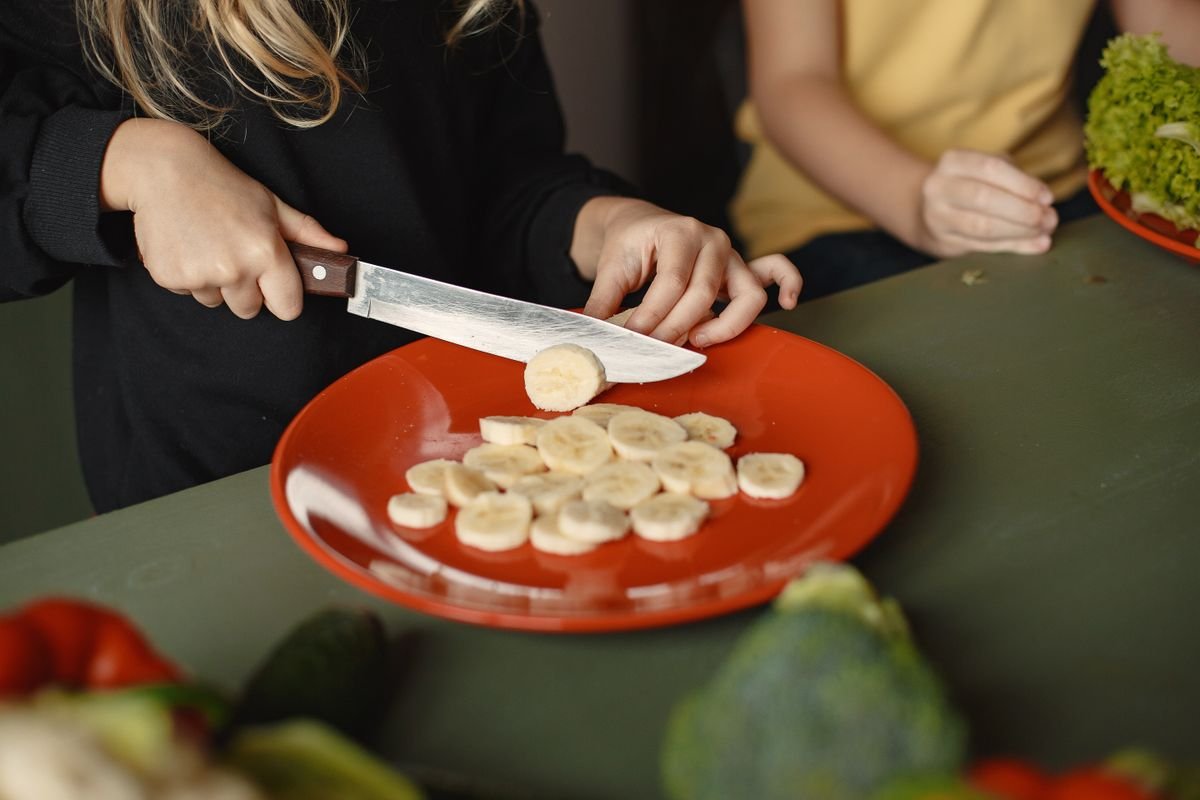 Chicos preparando rodajas de banana en la cocina como snack saludable